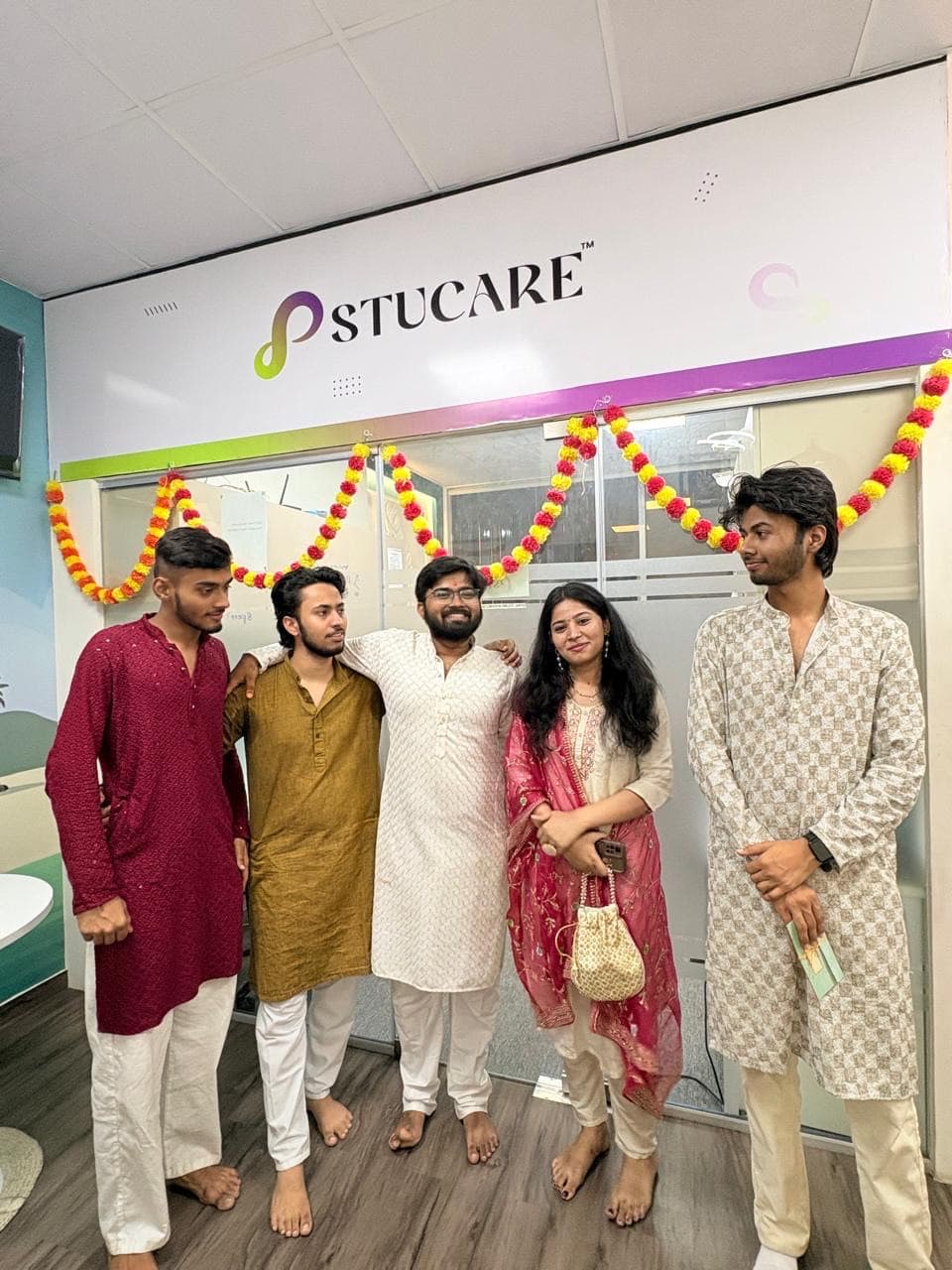Five members of the Stucare team in festive dress under the Stucare office signage, with marigold garlands strung across the entrance for Diwali.